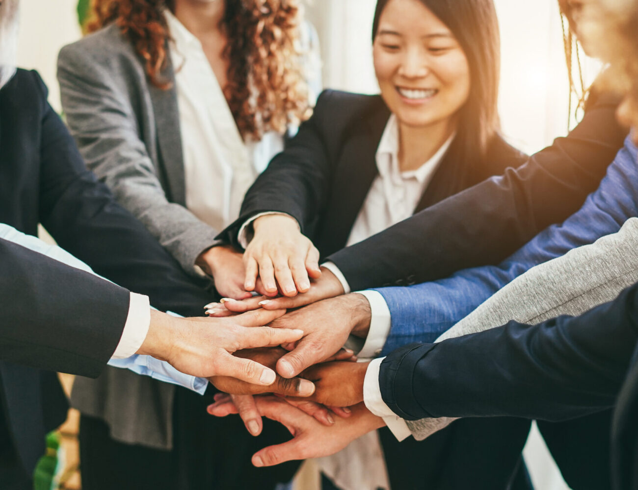 Multiracial business people celebrating together stacking hands inside modern office - Focus on center hands